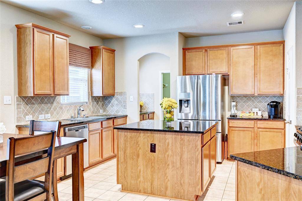 This kitchen features warm wood cabinetry, granite countertops, and a central island. It includes stainless steel appliances, a tiled backsplash, and ample natural light, creating a welcoming and functional space.