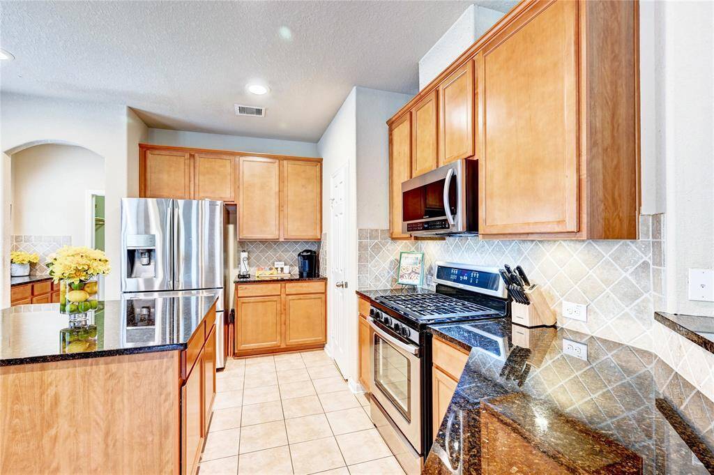 This kitchen features modern stainless steel appliances, ample wooden cabinetry, and sleek granite countertops. The tiled backsplash adds a touch of elegance, while the open layout provides a welcoming and functional space.