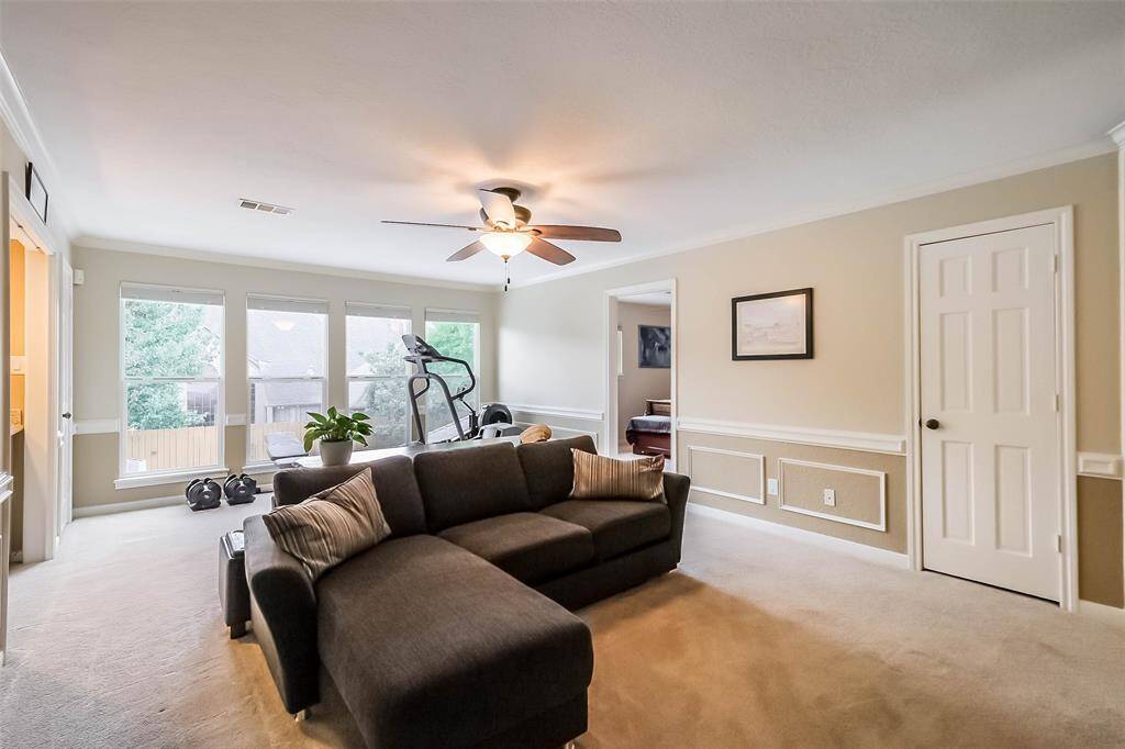 The upstairs game room features plush carpet ceiling fan, and large windows.