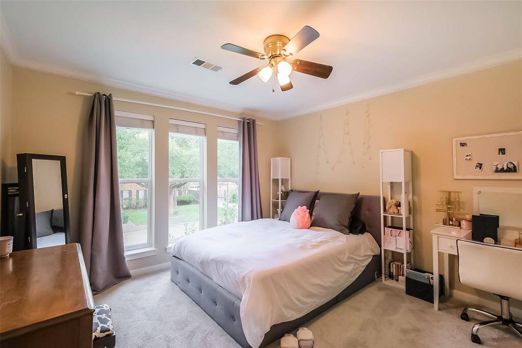 Fourth bedroom features largewindows, crown molding, ceiling fan, and plush carpet.