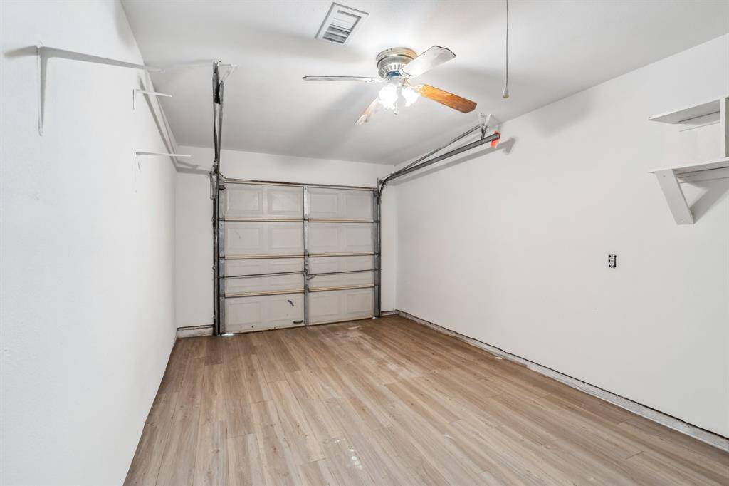 This angle highlights the full depth of the garage with continued wood-look flooring and ceiling fan, adding comfort to this flexible-use space. A roll-up door ensures it remains functional for vehicle storage if preferred.