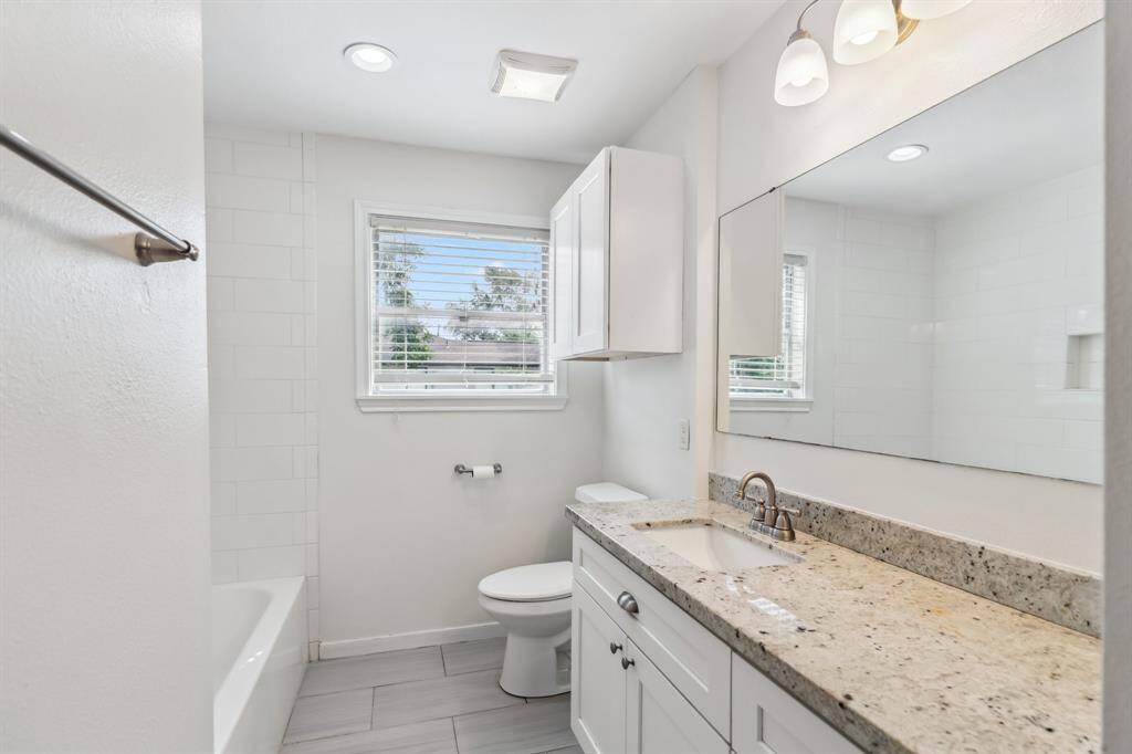 The updated secondary bath features a granite-topped vanity, updated lighting, and a window for natural ventilation. A deep soaking tub with tile surround completes this fresh, clean space.