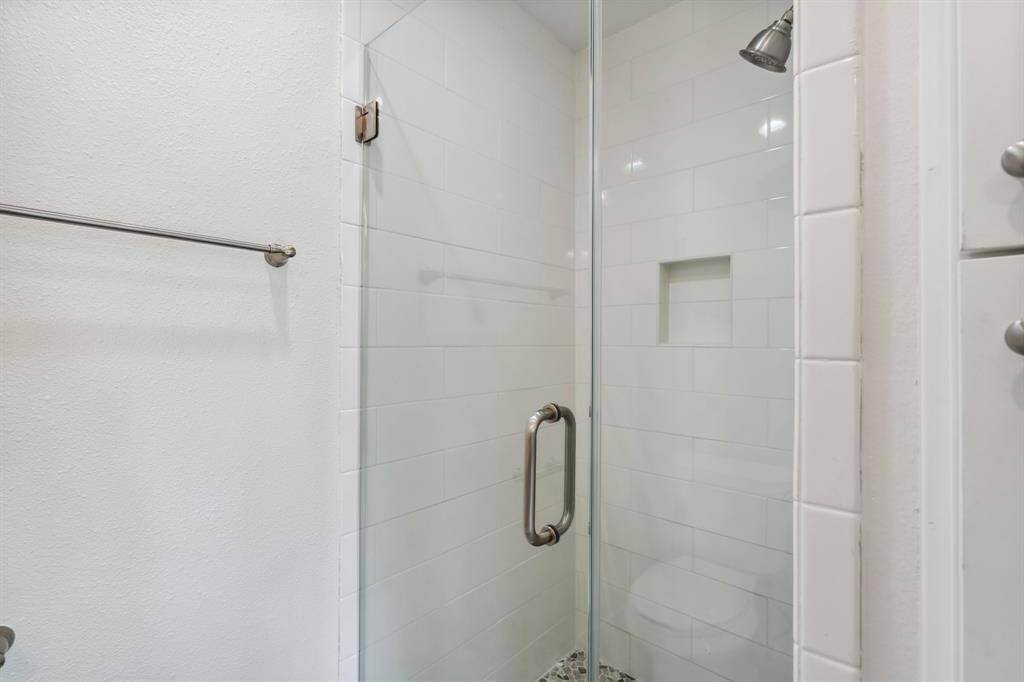 The updated walk-in shower features sleek white tile, built-in shelving, and a clear glass door for a modern touch. Thoughtful finishes make this bathroom feel clean and refreshed.