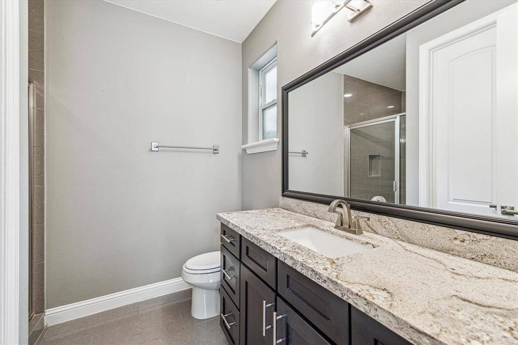 The first-floor guest suite includes a private ensuite bath with an extended single-sink vanity offering excellent storage, a framed mirror with stylish lighting above, and a convenient fully tiled walk-in shower.