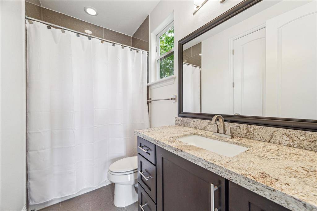 The ensuite bathroom features a granite-topped single-sink vanity with a framed mirror and overhead lighting, along with a fully tiled tub/shower combination for added convenience.