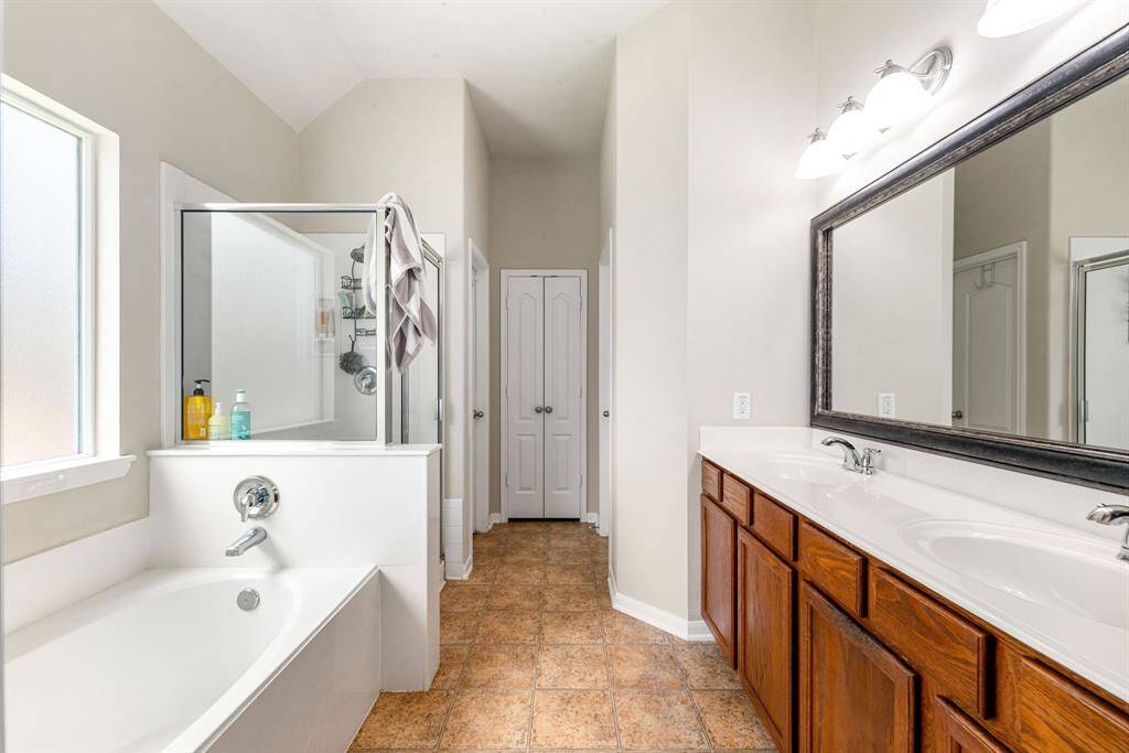 This primary bathroom is definitely move-in ready! Featuring a dark framed walk-in shower with tile surround, separate garden tub for soaking after a long day with custom tile detailing, dark stained cabinets with light countertops, spacious walk-in closet with shelving, high ceilings, custom paint, sleek and dark modern finishes.