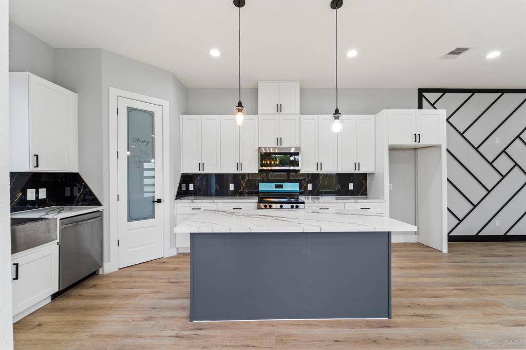Large kitchen island with pendant lights and stainless steel appliances
