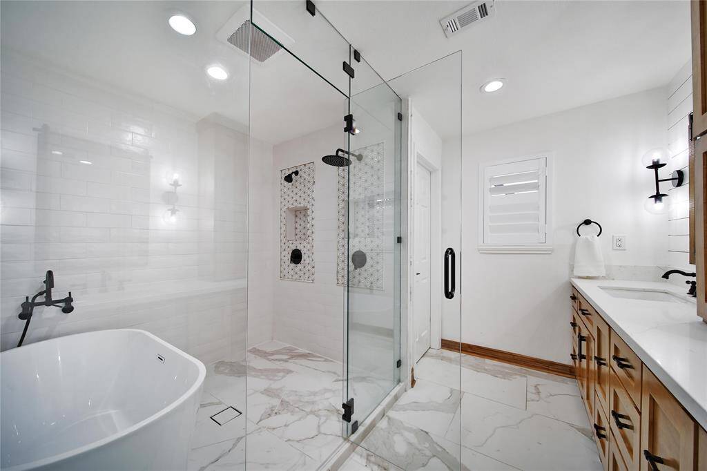"Wet room" bathroom is on point with designer trends. It features a fully enclosed glass space that houses both a freestanding tub and a separate shower area, creating a seamless, spa-like design.