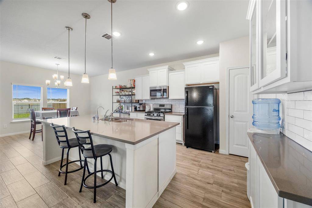 This photo showcases a modern kitchen with an open layout, featuring a spacious island with seating, pendant lighting, and white cabinetry. The kitchen flows into a dining area with large windows, providing ample natural light.