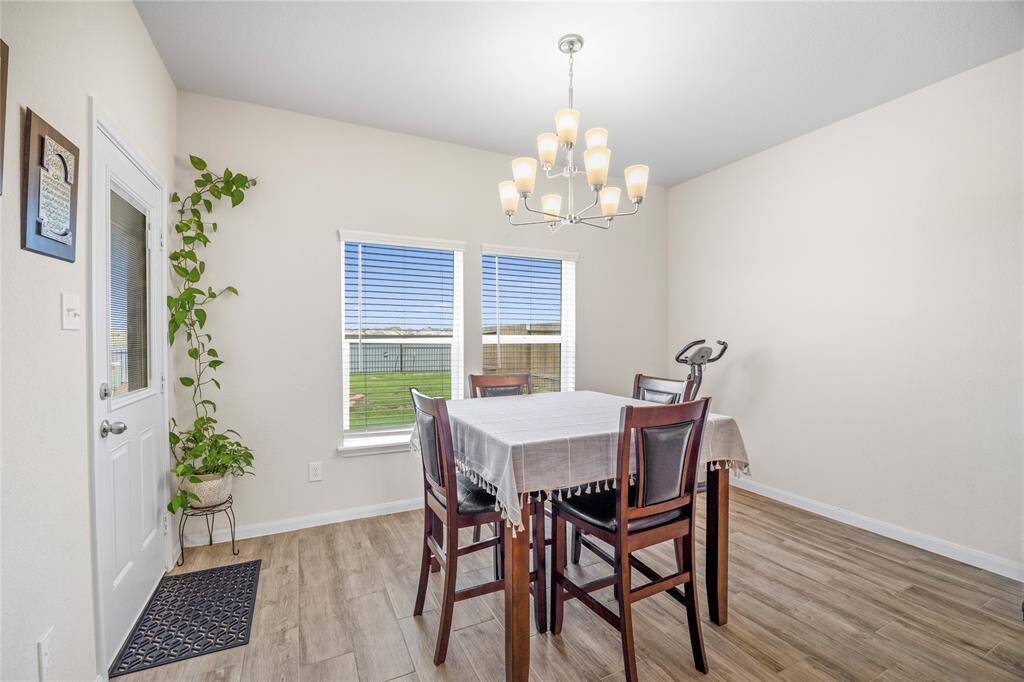 Bright dining area with a modern chandelier, wood flooring, and large windows that offer plenty of natural light. Features a cozy table setup and a door leading outside to the large backyard and a beautiful view of the lake..