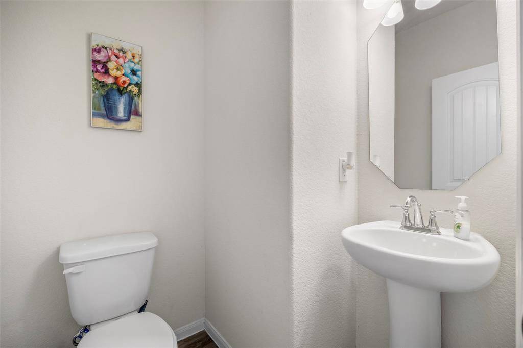 This is a small, bright bathroom featuring a pedestal sink, a toilet, and a wall mirror. It has a simple decor with neutral walls, creating a clean and inviting space for your decor.