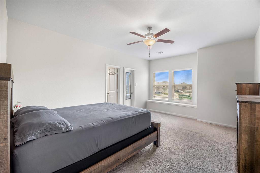 This is a spacious and bright primary bedroom featuring neutral carpet, and a ceiling fan. It has two windows allowing plenty of natural light, and a door leading to the ensuite. The room exudes a clean, modern feel.