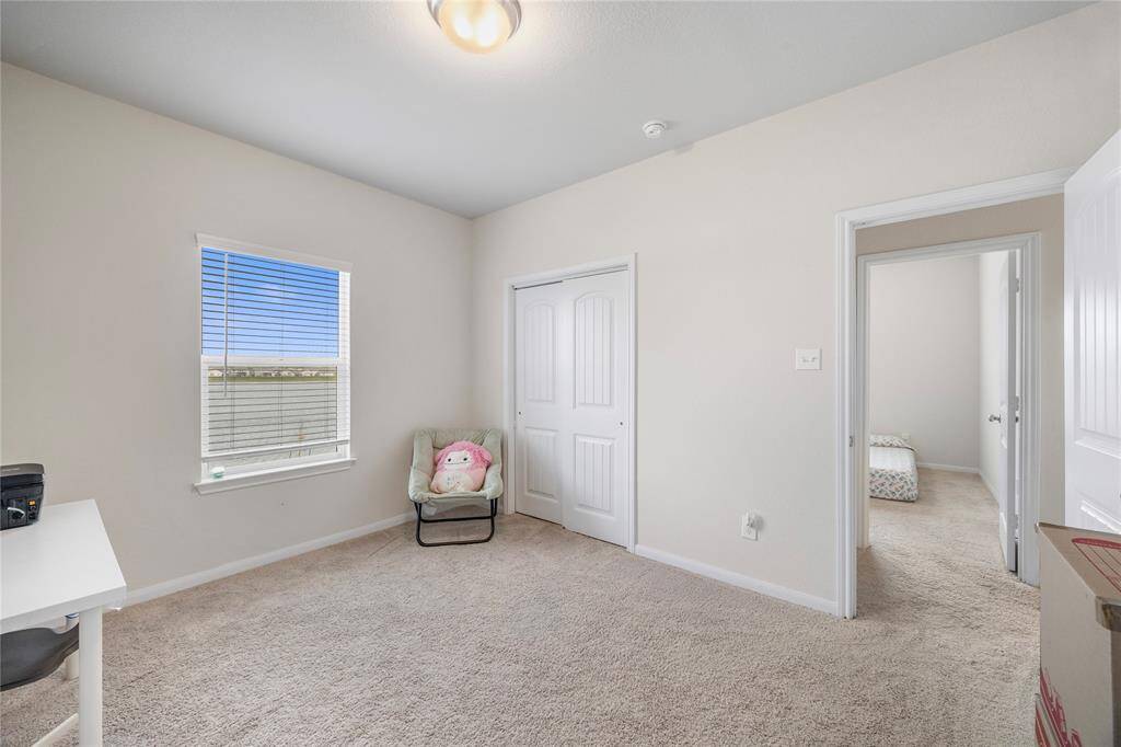 This is a cozy, carpeted bedroom with neutral walls, featuring a window for natural light, a small closet with double doors, and an adjoining room. It's versatile for various uses.