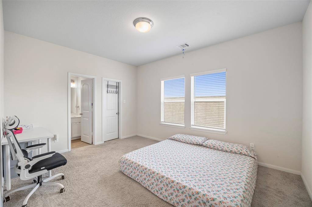 This bedroom features neutral walls and carpeting, a large window for natural light, and an en-suite bathroom. There is a desk area, making it versatile for work or study.