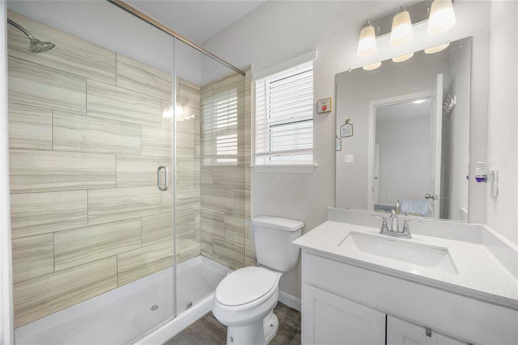 This modern bathroom features a sleek glass-enclosed shower with stylish tile, a contemporary vanity with ample counter space, and bright lighting. A window provides natural light, enhancing the clean, fresh look.