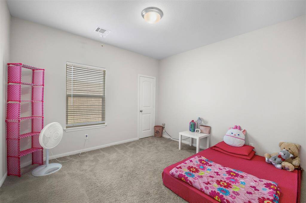 This is a simple, cozy bedroom with neutral walls and carpet. It features a small window, a white door, and a ceiling light. Perfect for a child or guest room.