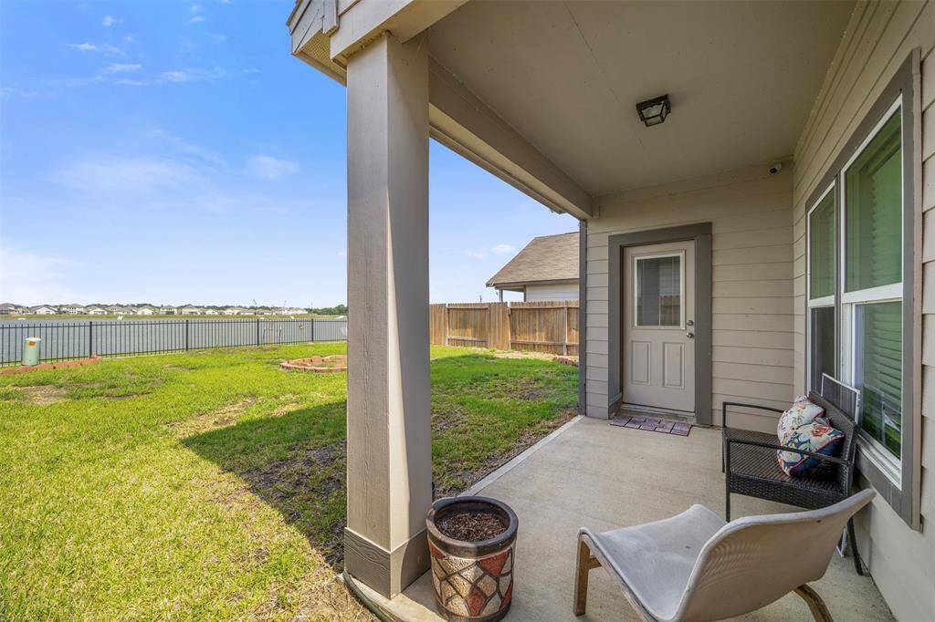 Charming covered patio with seating area, overlooking a spacious backyard with a view of a serene lake, perfect for relaxing or entertaining.