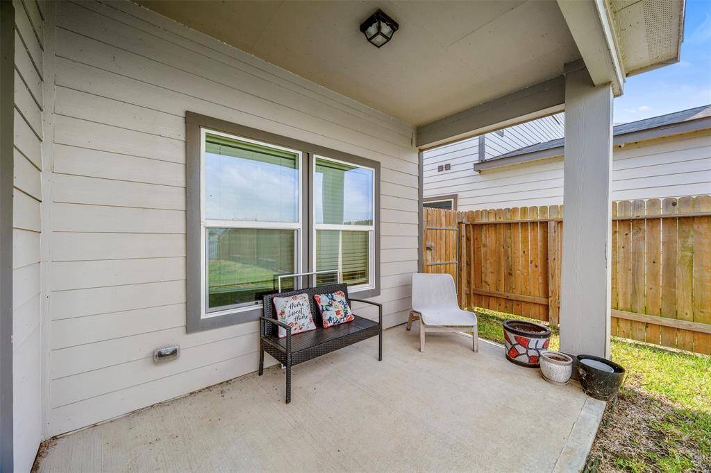 This photo showcases a cozy, covered patio bordered by a wooden fence. Ideal for outdoor relaxation, it features concrete flooring and space for potted plants.