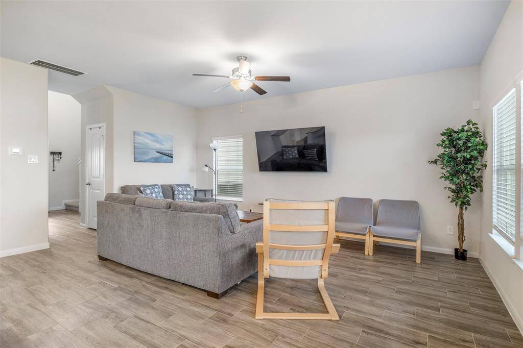 This spacious and bright living room features a modern design with neutral walls, wood-look tile flooring, and ample natural light, creating a welcoming atmosphere.