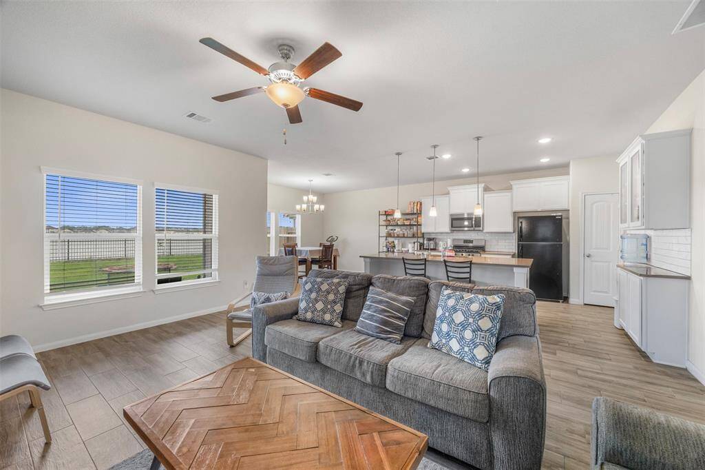 This open-concept living area features a cozy seating arrangement, a modern kitchen with a breakfast bar, and ample natural light from large windows overlooking a spacious backyard.