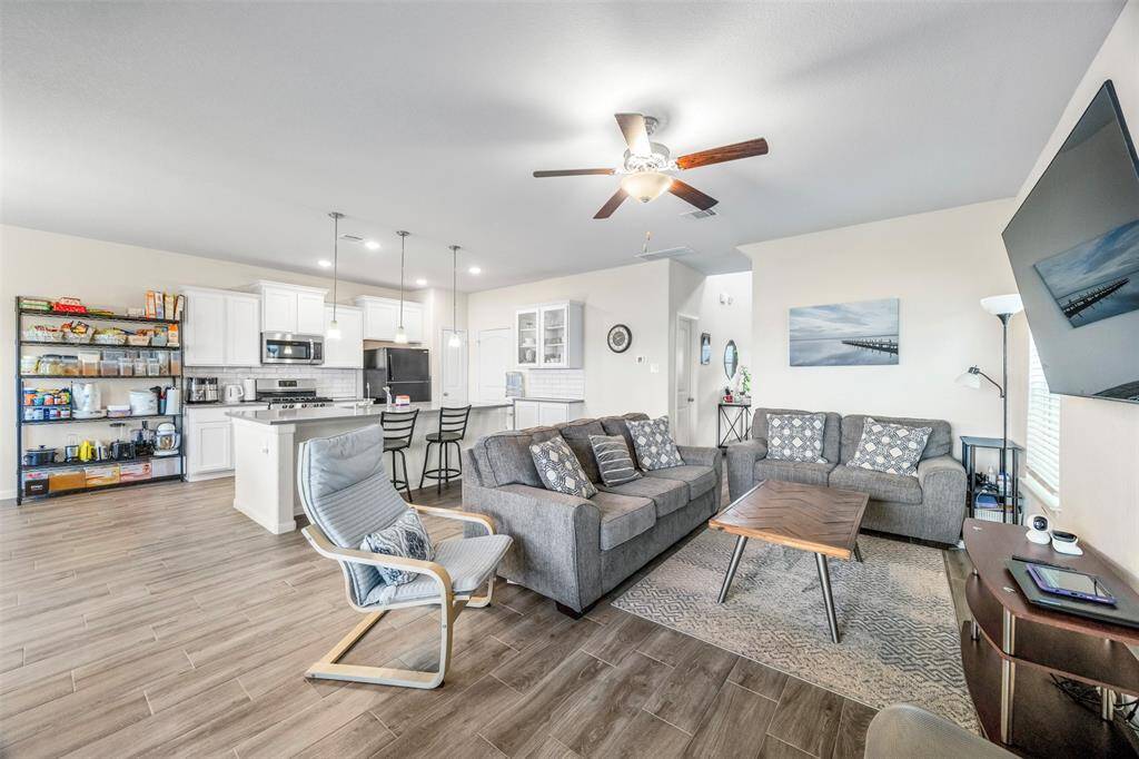 Another view of the living area, kitchen, and dining space. The room is bright with natural light from large windows, and a ceiling fan adds comfort. Perfect for entertaining and family gatherings.