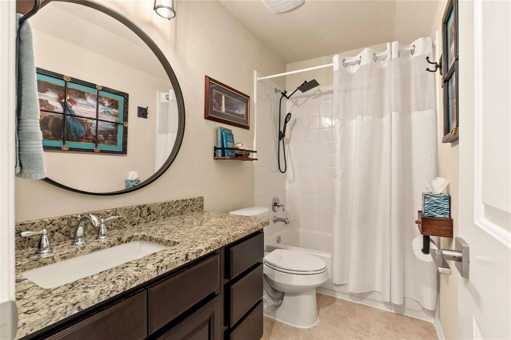 Upstairs full bathroom features a modern design with a granite countertop and dark wood cabinetry. It includes a shower-tub combo with round mirror and bright lighting.