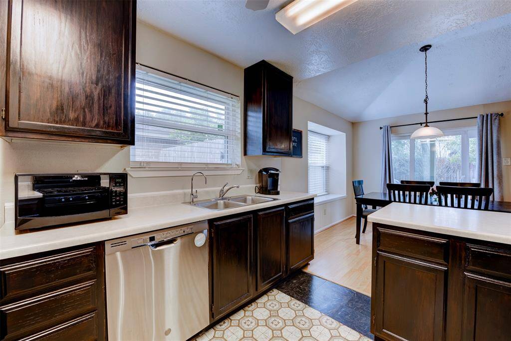 Kitchen features ample cabinet storage, an oversized window above the sink, expansive white Formica countertops, durable vinyl flooring, a breakfast bar for casual seating, and a recently purchased dishwasher for added convenience.