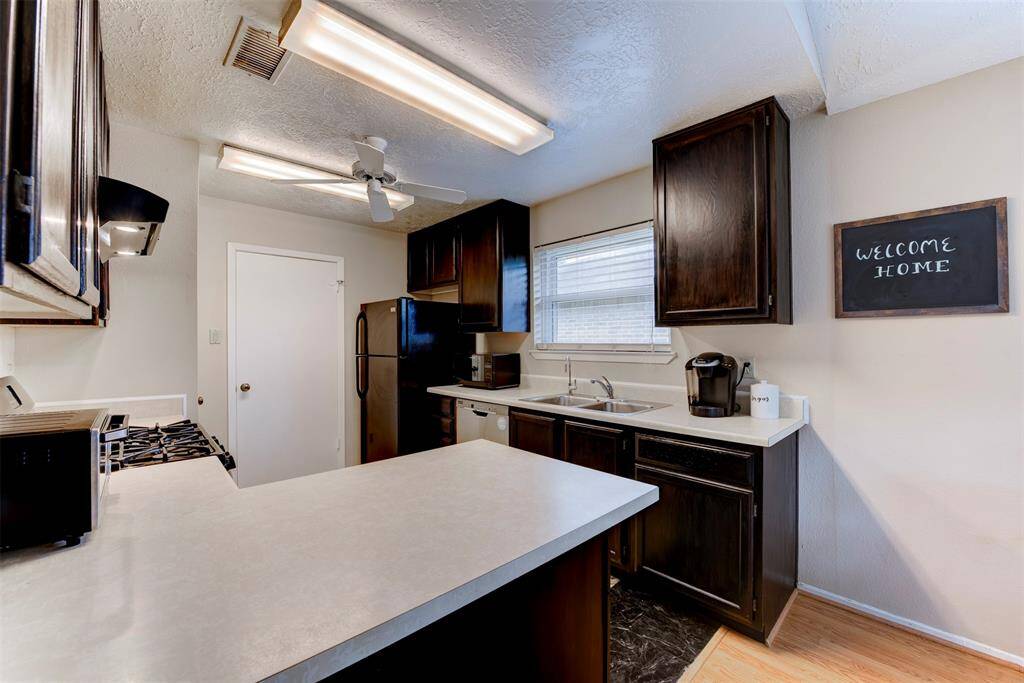 Alternate kitchen view showcasing excellent airflow with a ceiling fan, abundant natural light paired with oversized fixtures, and a stylish contrast between white countertops and dark wood cabinetry. Window above the sink brings in additional light and charm.