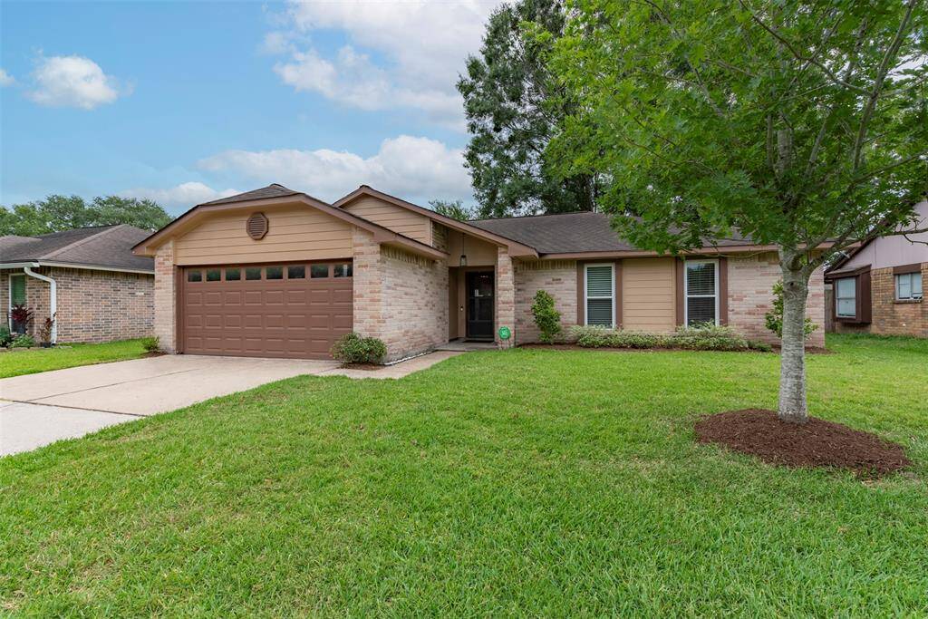 Alternate view of the charming brick exterior with siding accents, nestled under a mature tree with a manicured lawn, vibrant flower beds, and a private double-wide driveway.