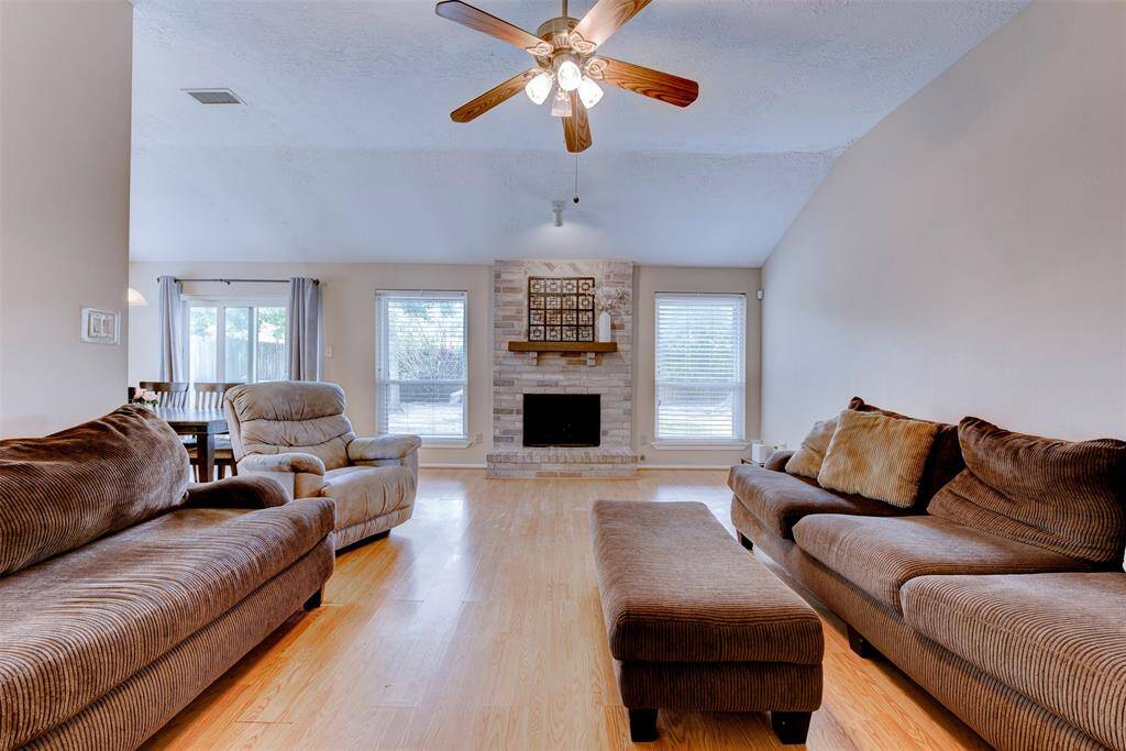 Expansive living room designed for both relaxing and entertaining, featuring durable vinyl flooring, a central gas fireplace, oversized double-pane windows, and a ceiling fan with light kit.