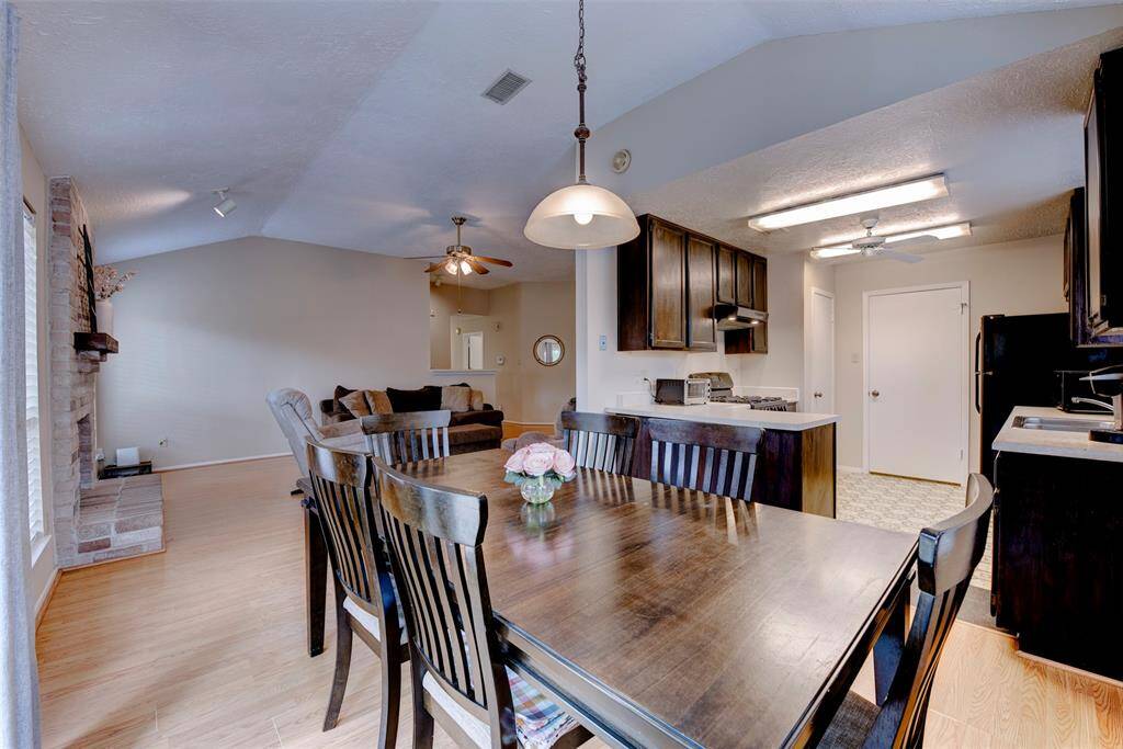 Spacious dining area comfortably fits a table for 6 to 8, anchored by a duo inverted bowl light fixture. Tall ceilings, abundant natural light, and durable vinyl flooring complete the space.