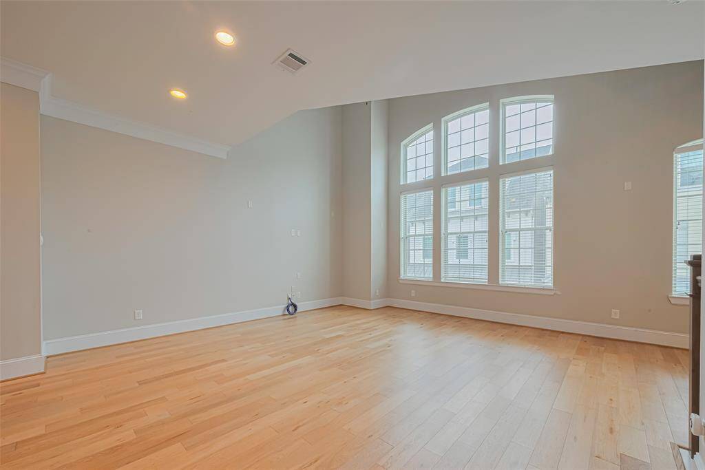 Spacious and light-filled living area featuring vaulted ceilings, oversized arched windows, and warm hardwood floors. This open-concept space offers endless possibilities for your ideal layout and design.