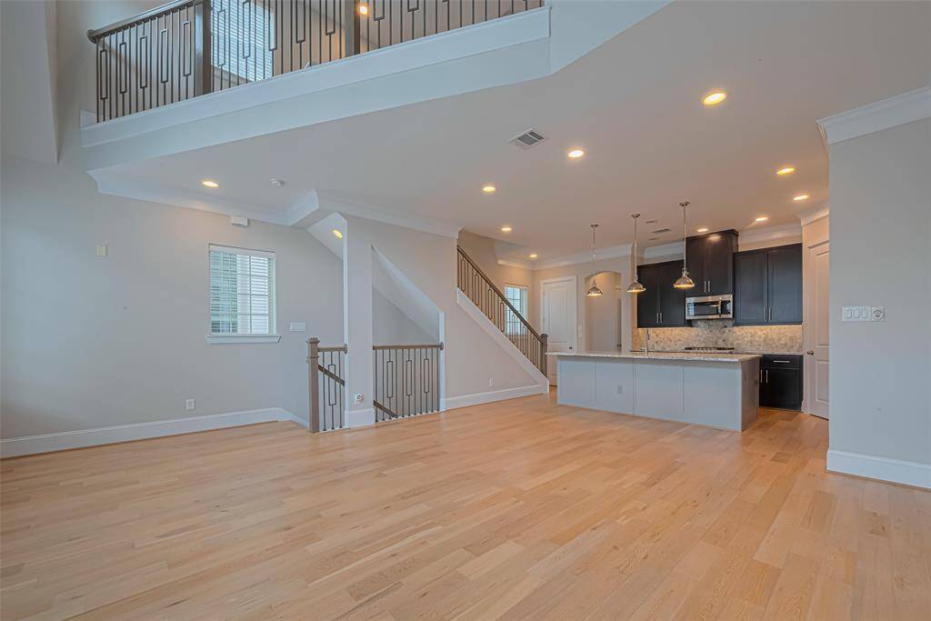 Open-concept living, dining, and kitchen area featuring soaring ceilings, rich wood floors, and abundant natural light. The chef’s kitchen is equipped with granite countertops, a large island with pendant lighting, and sleek dark cabinetry. Modern iron stair railings and crown molding add stylish finishing touches to this bright and versatile space.