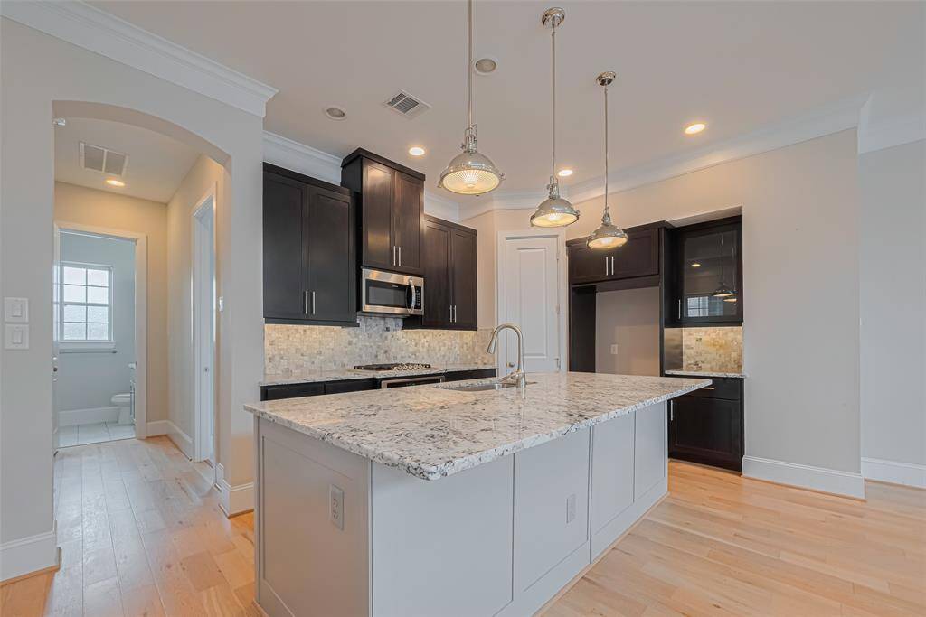 Gourmet kitchen featuring a large granite island with breakfast bar seating, custom dark wood cabinetry, and a stylish tile backsplash. Pendant lighting, stainless steel appliances, and two walk-in pantry complete this elegant and functional space—ideal for both cooking and entertaining.