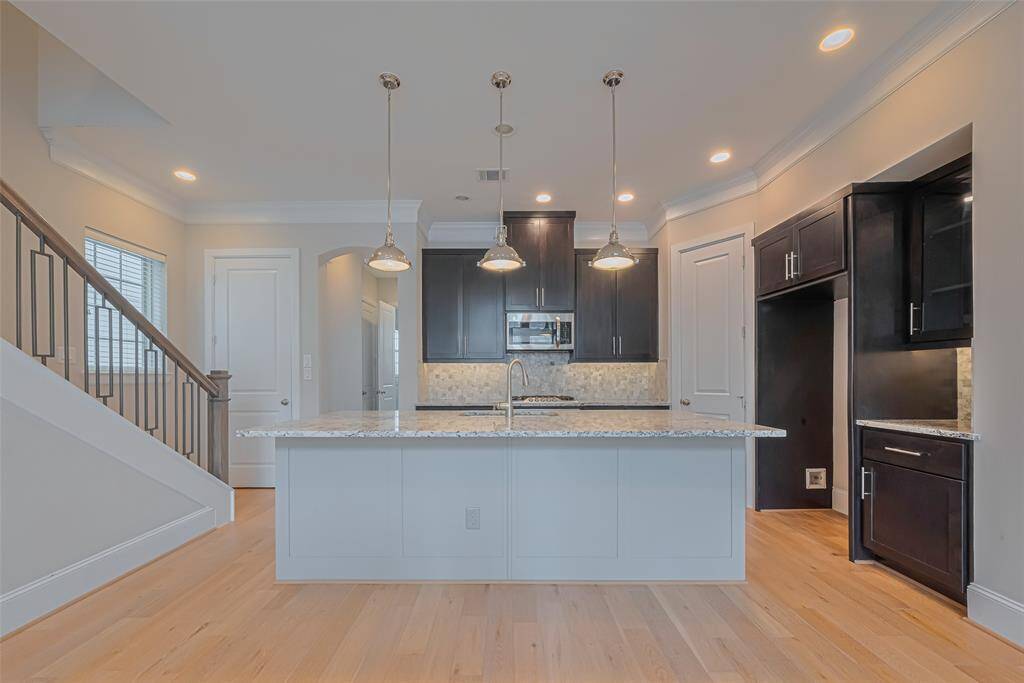 Stunning chef’s kitchen with a large center island, pendant lighting, granite countertops, and sleek dark cabinetry. The open layout flows effortlessly into the main living area, while stainless steel appliances and a mosaic tile backsplash add a modern touch to this beautifully designed space.