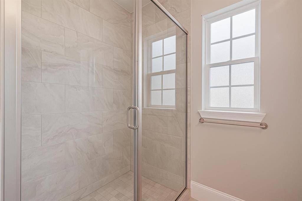 This beautifully tiled walk-in shower features a seamless glass door, large-format porcelain tiles with natural stone texture, and a frosted window that brings in soft natural light while maintaining privacy. A sleek, modern design ideal for both guests and everyday comfort.