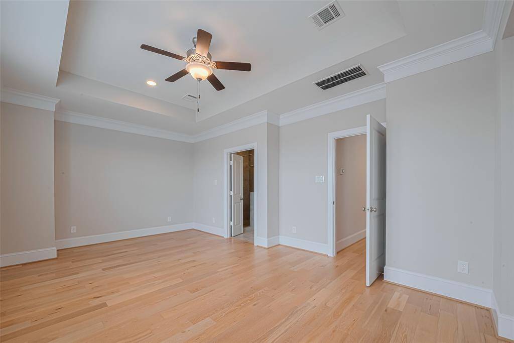 The 3rd-floor Primary Bedroom offers a spacious, private retreat featuring a high tray ceiling with crown molding and elegant hardwood flooring. The open layout provides plenty of room for a sitting area or additional furniture. Enjoy the natural light, ceiling fan comfort, and quiet privacy with no other rooms on this level.