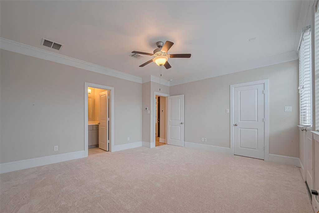 This first floor bedroom offers a spacious layout with plush new carpet, double crown molding, and a ceiling fan for comfort. The room includes an en-suite full bathroom, and ample closet space.