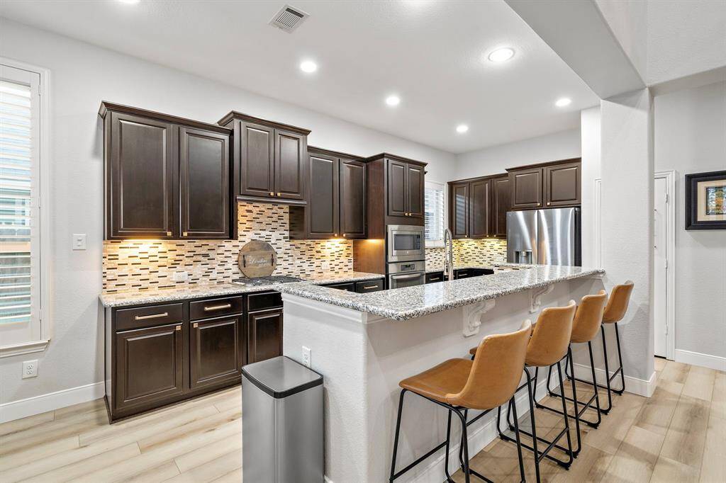 The stylish tile backsplash blends neutral tones, beautifully complementing the granite countertops and cabinetry. Elegant under-cabinet lighting illuminates the workspace, creating a warm and inviting atmosphere for cooking.