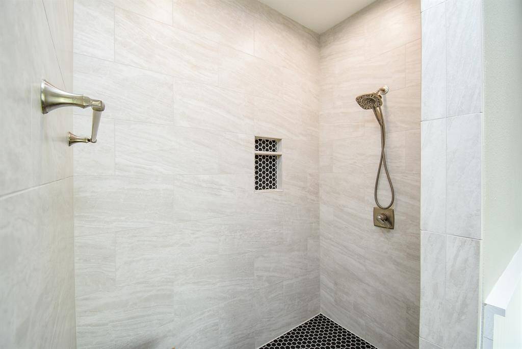 Oversized shower with designer wall tile, accented tile inset shelf with matching flooring, handheld shower head and bright light.