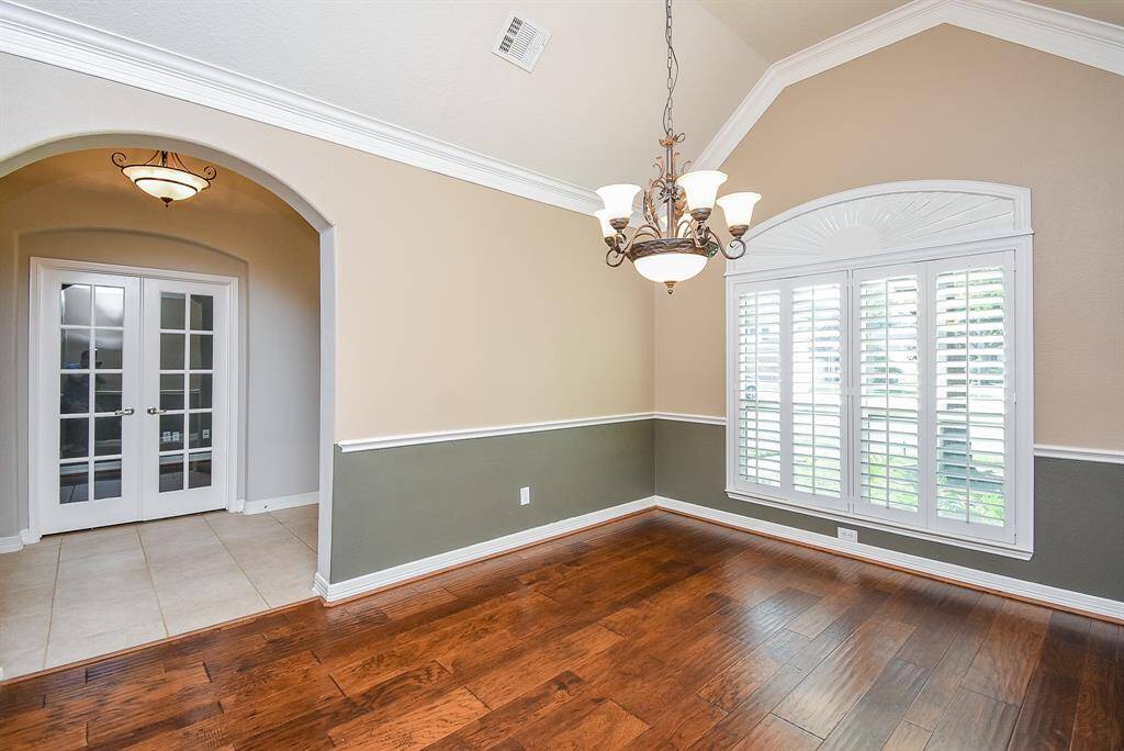 Elegant arched opening into the dining room with custom chandelier, wood flooring, wall of windows with custom Shutters, Wainscoting and crown molding displays the elegance carried throughout the home.