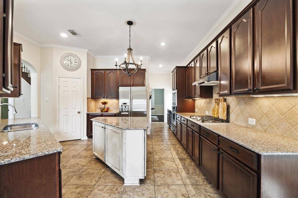 This spacious kitchen features a sophisticated design with rich, dark cabinetry, gas stovetop and a large center island topped with granite countertops, offering plenty of counter space to entertain and create your culinary masterpieces.