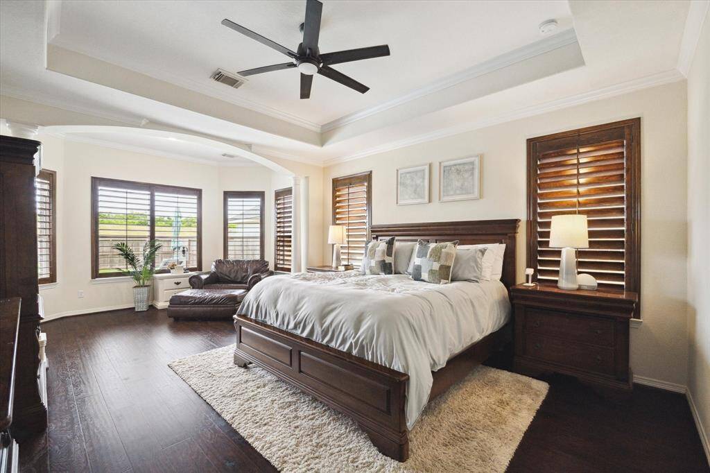 A spacious primary bedroom bathed in natural light, streaming through large windows framed by plantation shutters. The space features a door directly to the outside with direct access to the spa as well as a sitting area near the windows, ideal for unwinding with views of the outdoor oasis.