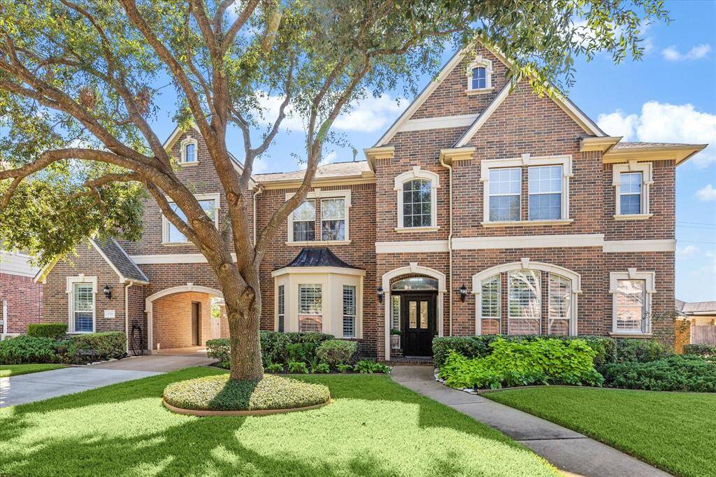 This beautiful brick home features a classic, elegant design with large windows and a well-maintained front yard. A mature tree provides shade, complementing the lush landscaping offering great curb appeal.