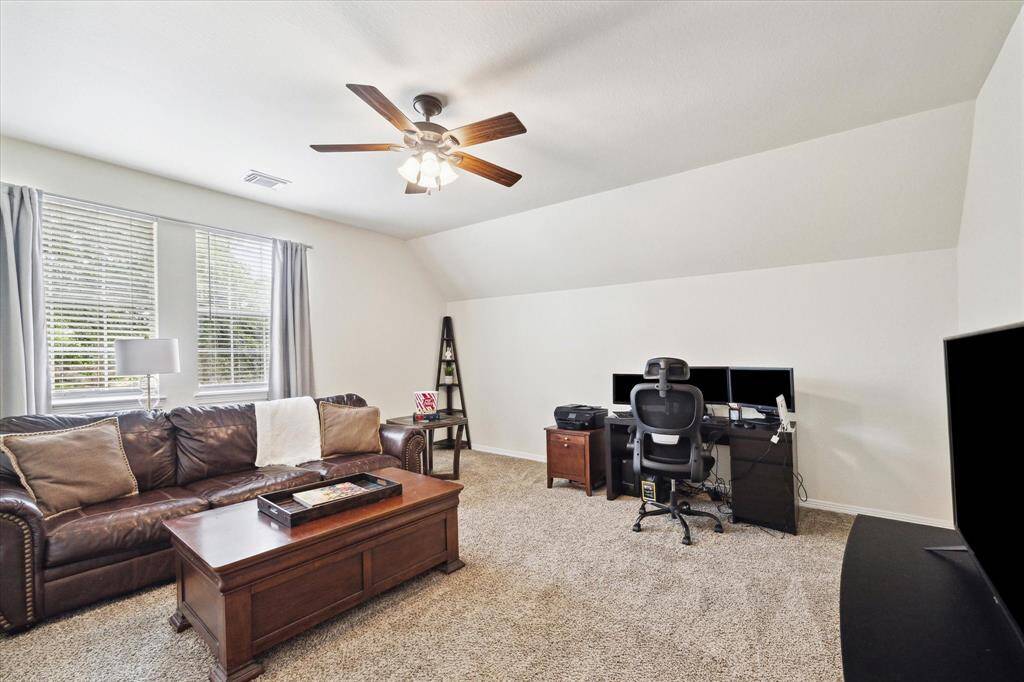A versatile media room with a spacious, open layout, complemented by a sloped ceiling that adds architectural interest. The room is finished with neutral walls and plush carpeting, creating a warm and inviting atmosphere ideal for entertainment or relaxation.