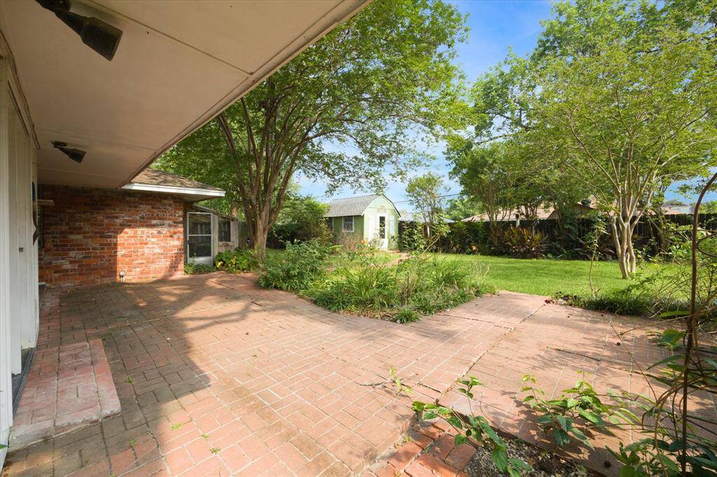 The backyard is beautifully landscaped. You can see the green workshop and the door to the greenhouse right next to the brick wall.  There is still room for a pool!