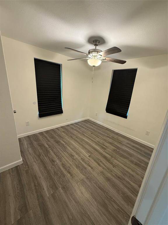 Another bedroom where tall windows frame the outdoors and a ceiling fan offers cool circulation. The consistent flooring throughout adds unity and flow to the interior layout.
