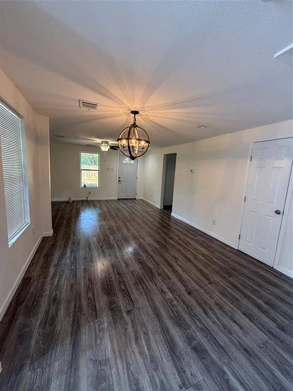 Through the front door, a seamless transition into an airy living area welcomes you with tall windows that brighten the space. The ceiling fan above and gleaming floors below create a harmonious balance of comfort and refinement. Adjacent, a striking light fixture over the dining space draws the eye inward.