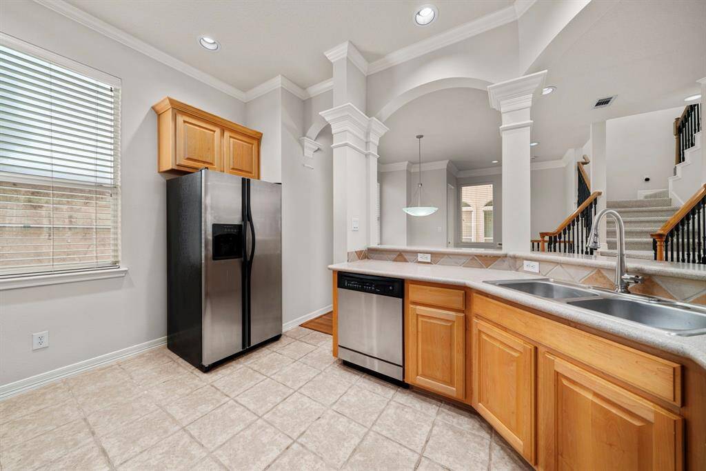 This kitchen features a smart layout with stainless steel appliances, tile flooring, and plenty of counter space. Decorative archways and crown molding add a touch of architectural charm while opening the view into the adjacent dining and living spaces.
