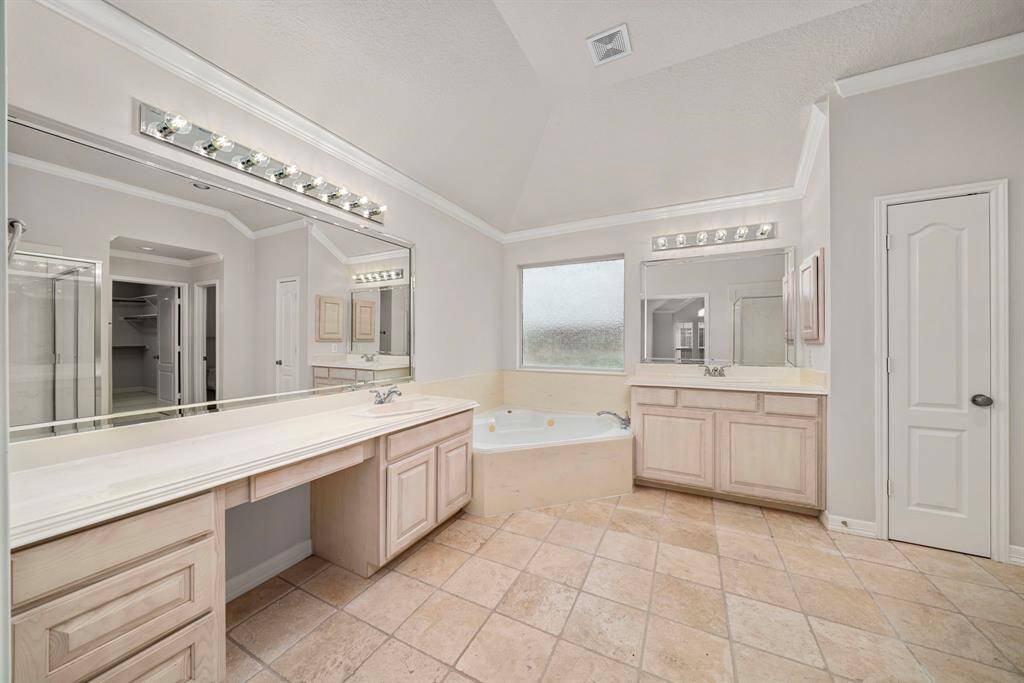 The spacious primary bathroom features dual vanities, a large jetted soaking tub, and expansive mirrors for added light and function. Ample cabinetry and counter space provide excellent storage.
